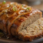 A sliced French onion meatloaf topped with caramelized onions and glaze, served on a rustic plate.